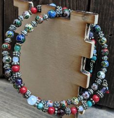 two bracelets with colorful beads and charms on top of a wooden box next to a door