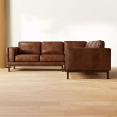 a brown leather couch sitting on top of a hard wood floor next to a white wall