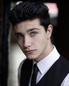 a young man wearing a black vest and white shirt is looking at the camera with an intense look on his face