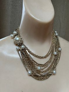 "Wonderful statement necklace for the woman who takes her necklaces seriously.   No name but truly, not needed. Total 12 chains with 2 strands featuring creamy ivory faux pearls about 8mm each. Variety of delicate goldtone chains in different sizes.  Most are a variation of curb links, some textured. Lovely large slide insert clasp to position as you like, perhaps on the side/front of the body.  Clasp measures 1\" diameter. I usually offer coodinating earrings but the ones I have are very large Elegant Pearl Chain Layered Choker Necklace, Multi-strand Layered Pearl Chain Necklace For Parties, Multi-strand Layered Pearl Necklace For Party, Multi-strand Gold Pearl Chain Jewelry, Gold Multi-strand Pearl Chain Jewelry, Elegant Multi-strand Pearl Necklace, Elegant Double Strand Pearl Chain Layered Necklace, Elegant Double Strand Layered Necklace With Pearl Charm, Elegant Double Strand Pearl Layered Necklace