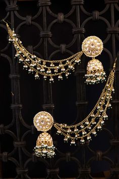 a gold necklace and earring set with pearls on the sides, hanging from a wrought iron fence