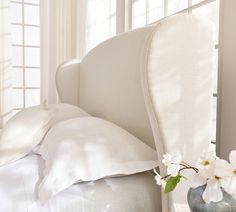 a bed with white linens and pillows on it next to a vase with flowers