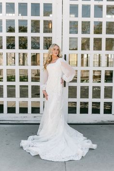 a woman standing in front of a white door wearing a long sleeved wedding dress