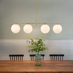 a dining room table with four lights hanging from it's ceiling and flowers in a vase on the table