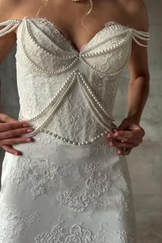 a woman in a white wedding dress with pearls on the shoulders and shoulder, holding her hands behind her back