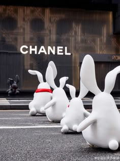 three white rabbits sitting in front of a chanel store on the side of a street