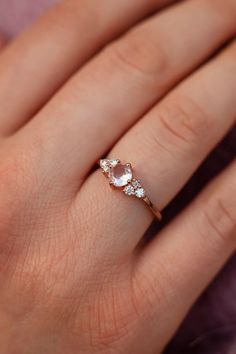 a woman's hand with a diamond ring on top of her finger and an oval pink stone in the middle