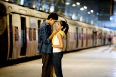 a man and woman standing next to each other on a train platform at night time