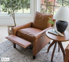 a living room with a chair, lamp and table in front of a window that looks out onto the yard