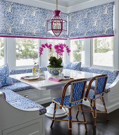 a dining room table with blue and white patterned chairs next to a window covered in roman shades