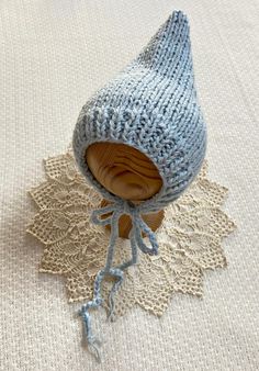 a knitted blue hat on top of a wooden doll's head, sitting on a lace doily