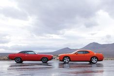 two orange cars parked next to each other on a wet parking lot with mountains in the background