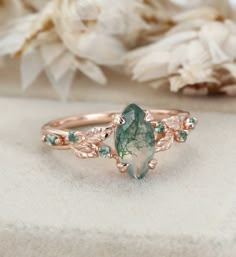 Celebrate the beauty of nature with this Nature-Inspired Marquise Cut Moss Agate Engagement Ring. Crafted in vintage rose gold, this ring features a stunning marquise-cut moss agate centerpiece, complemented by an elegant twist leaf design on the band. Perfect for engagements, weddings, or anniversaries, this unique piece is a thoughtful gift for someone who cherishes organic and timeless designs. Tree Agate Ring, Earthy Engagement Rings Nature, Leaf Wedding Band With Engagement Ring, Simple Moss Agate Engagement Ring, Whimsical Rings Engagement, Engagement Rings Organic, Vintage Inspired Engagement Rings Unique, Nature Themed Wedding Rings, Vintage Floral Engagement Ring