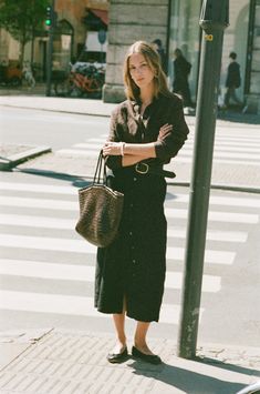 a woman standing next to a street sign holding a brown bag and wearing black shoes