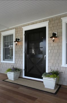 two planters on the front porch of a house with white trim and black doors