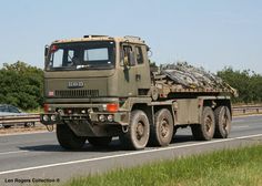 an army truck is driving down the road with another car in the distance behind it