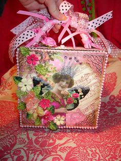 a box that is decorated with flowers and ribbons on top of a red table cloth