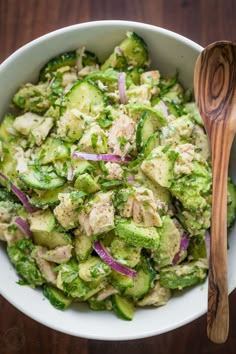 a white bowl filled with cucumber and chicken salad next to a wooden spoon