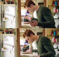 the young man is looking at his cell phone while standing in front of an open refrigerator