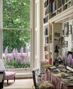 a room with lots of bookshelves and purple flowers in the window sill