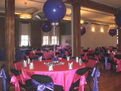 a room filled with lots of tables covered in purple and black cloths next to balloons