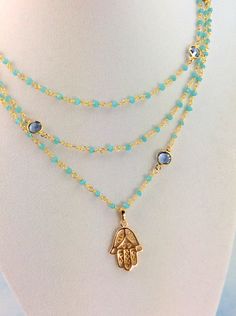 "This is a very lovely 18kt gold filled Hamsa pendant with three layers of 2-3mm faceted Aqua Chalcedony gemstones on 24kt gold vermeil.  Beautiful Blue Swarovski crystals are scattered throughout this necklace.  Pendant measures 25x17mm.  The color combination is breath taking even more beautiful in person.  Necklace layers measure 16\"-18\" ,  18-20\"  or  20\"-22\".  Please choose size.  Necklace comes with a gold filled toggle closure.  Comes nicely boxed for the perfect gift! PLEASE READ... Gold Faceted Necklaces For Layering, Gold Crystal Necklaces With Faceted Beads For Layering, Gold Gemstone Crystal Necklace For Layering, Gold Double Strand Crystal Necklace With Natural Stones, Gold Double Strand Crystal Necklace With Faceted Beads, Gold Faceted Multi-strand Jewelry, Spiritual Multi-strand Gemstone Necklaces, Gold Multi-strand Crystal Necklaces With Natural Stones, Handmade Gold Multi-strand Crystal Necklace