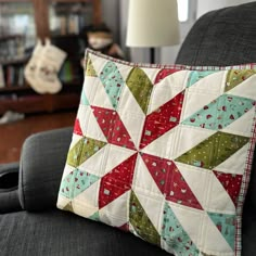 a patchwork pillow sitting on top of a gray couch next to a lamp and bookcase