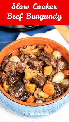 a bowl filled with beef and potatoes on top of a blue table cloth next to a pot