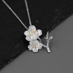 Introducing our exquisite pendant featuring a delicate design of cherry blossoms crafted in sterling silver. The intricate details of the flowers are beautifully highlighted with gold plating on the stamens, adding a touch of elegance and sophistication. The pendant captures the essence of spring, symbolizing renewal and beauty. It hangs gracefully from a matching sterling silver chain, making it a timeless accessory suitable for any occasion. Delicate Spring Jewelry For Anniversary, Delicate Jewelry For Spring Anniversary, Delicate Jewelry For Anniversary In Spring, Elegant Sterling Silver Spring Jewelry, Elegant Sterling Silver Jewelry For Spring, Spring Sterling Silver Jewelry With Flower Charm, Spring Sterling Silver White Jewelry, Spring White Sterling Silver Jewelry, Elegant Flower Necklace Spring Gift