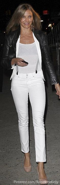 a woman in white pants and a black jacket is walking down the street at night