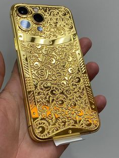 a hand holding a gold iphone case in it's left hand, with an intricate design on the back