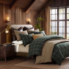 a bed with plaid comforter and pillows in a room next to a large window