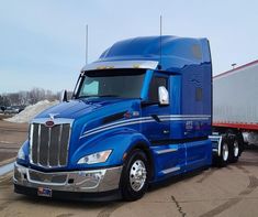 a blue semi truck parked in a parking lot next to a red and white trailer