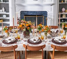 a dining room table set with plates and flowers in front of a fire place mantle