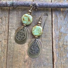 Boho brass and earthy green Czech glass dangle earrings.Small and lightweight, these brass earrings feature a small, swirled, earthy green and brown Czech glass bead and various shapes of brass dangles. The warm, light and neutral colors of these earrings make them a perfect everyday pair.Product overview:- Made with small Czech glass beads with various shapes of antiqued brass- Total hanging length of 2", the glass beads are approximately 0.5" in diameter- Very light weight and versatile- Hypoa Earthy Bronze Jewelry With Ear Wire, Earthy Bronze Earrings With Ear Wire, Rustic Brown Brass Earrings, Earthy Brass Jewelry With Ear Wire, Green Brass Earrings Nature-inspired, Earthy Green Dangle Earrings, Green Brass Earrings With Wire Wrapping, Green Patina Bohemian Earrings, Green Bohemian Earrings With Patina