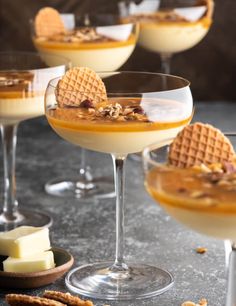 three glasses filled with dessert sitting on top of a table next to crackers and cheese