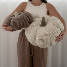 a woman holding two crocheted pumpkins in one hand and a stuffed animal in the other