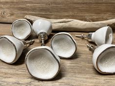 six white ceramic knobs on top of a wooden table next to a piece of driftwood