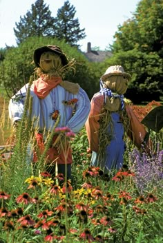 two scarecrows standing in the middle of a flower garden with lots of flowers