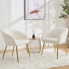 two white chairs sitting on top of a rug in front of a wall mounted painting