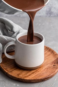 chocolate being poured into a white mug on a wooden plate with a gray and white towel