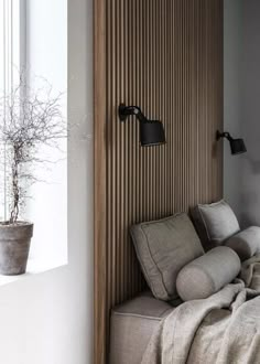 a bed sitting under a window next to a wooden headboard and wall mounted lamp