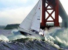 a sailboat is in the water near a large bridge and waves are around it