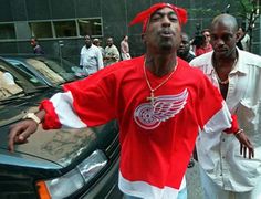 a man standing next to a black car in front of another man wearing a red and white shirt