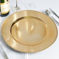 a gold plate with beaded edges sits on a table next to wine glasses and silverware