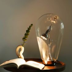 an open book sitting on top of a wooden table next to a vase and lamp