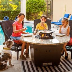 three children sitting around a table with food on it and a dog standing next to them