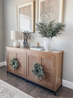 a sideboard with two vases on it and some greenery in the middle