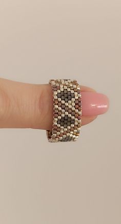 a woman's hand with a ring on it that is made out of gold and silver beads