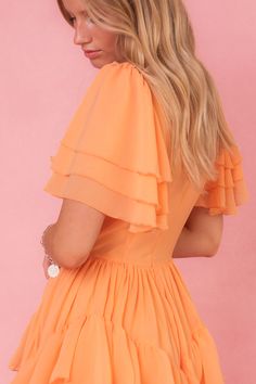 The Solana Dress in Apricot is a stunning piece that will elevate any wardrobe. Its unique features, including a square neckline, flutter sleeves, & a ruffle tiered skirt with pockets, make it both fashionable and functional. The hidden back zipper and functional front corset add a touch of elegance. With a non-stretch fabric and a lined bodice and skirt, this dress offers both comfort and style. Fitted Tiered Dress For Dress Down Occasions, Fitted Tiered Dress For Casual Wear, Spring Ruched Mini Dress With Flutter Sleeves, Tiered Ruffle Hem Dress, Flowy Tiered Ruffled Skirt Dress, Ruched Flutter Sleeve Dress For Garden Party, Flutter Sleeve Ruched Dress For Garden Party, Garden Party Dresses With Ruched Flutter Sleeves, Summer Ruffle Sleeve Dress For Casual Occasions